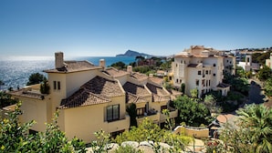 A coastal residential area with terracotta-tiled buildings, a clear sky, and a view of the sea. - Seafront Apartment with Pool, Sea Views, Wi-Fi & Air Conditioning (Altea)