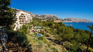 A coastal hotel with a pool, lush greenery, and a view of the sea and mountains. - Seafront Apartment with Pool, Sea Views, Wi-Fi & Air Conditioning (Altea)