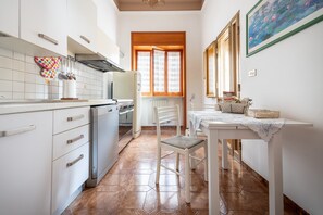 Una cocina con armarios blancos, una mesa de comedor con mantel blanco y una ventana con contraventanas de madera.