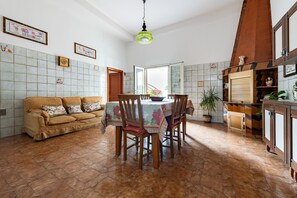 Uma sala de jantar com uma mesa posta para quatro pessoas, um sofá e uma cozinha com armários e um lustre.