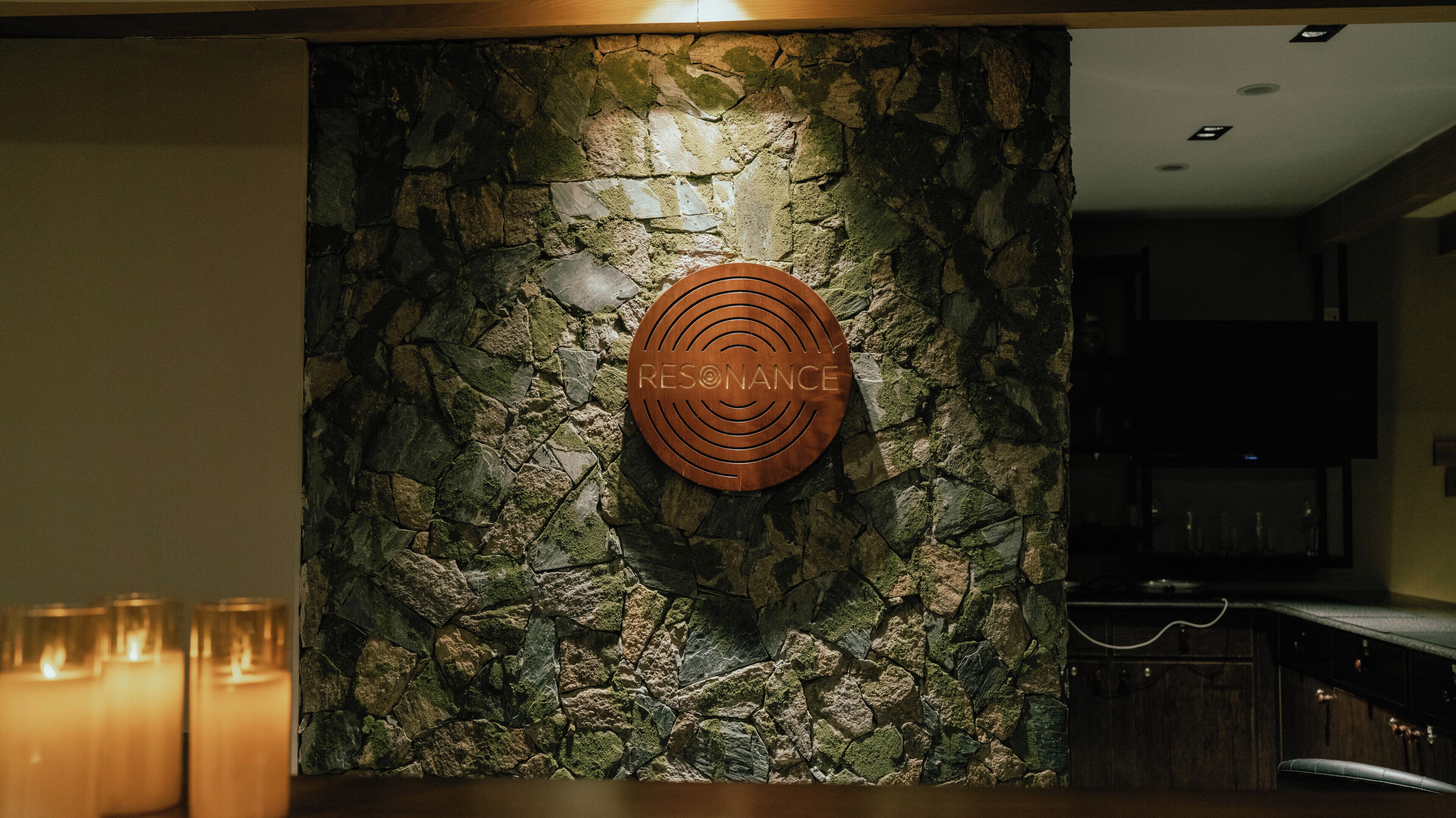 A stone wall with a circular sign reading 'RESONANCE' and a bar area with candles.