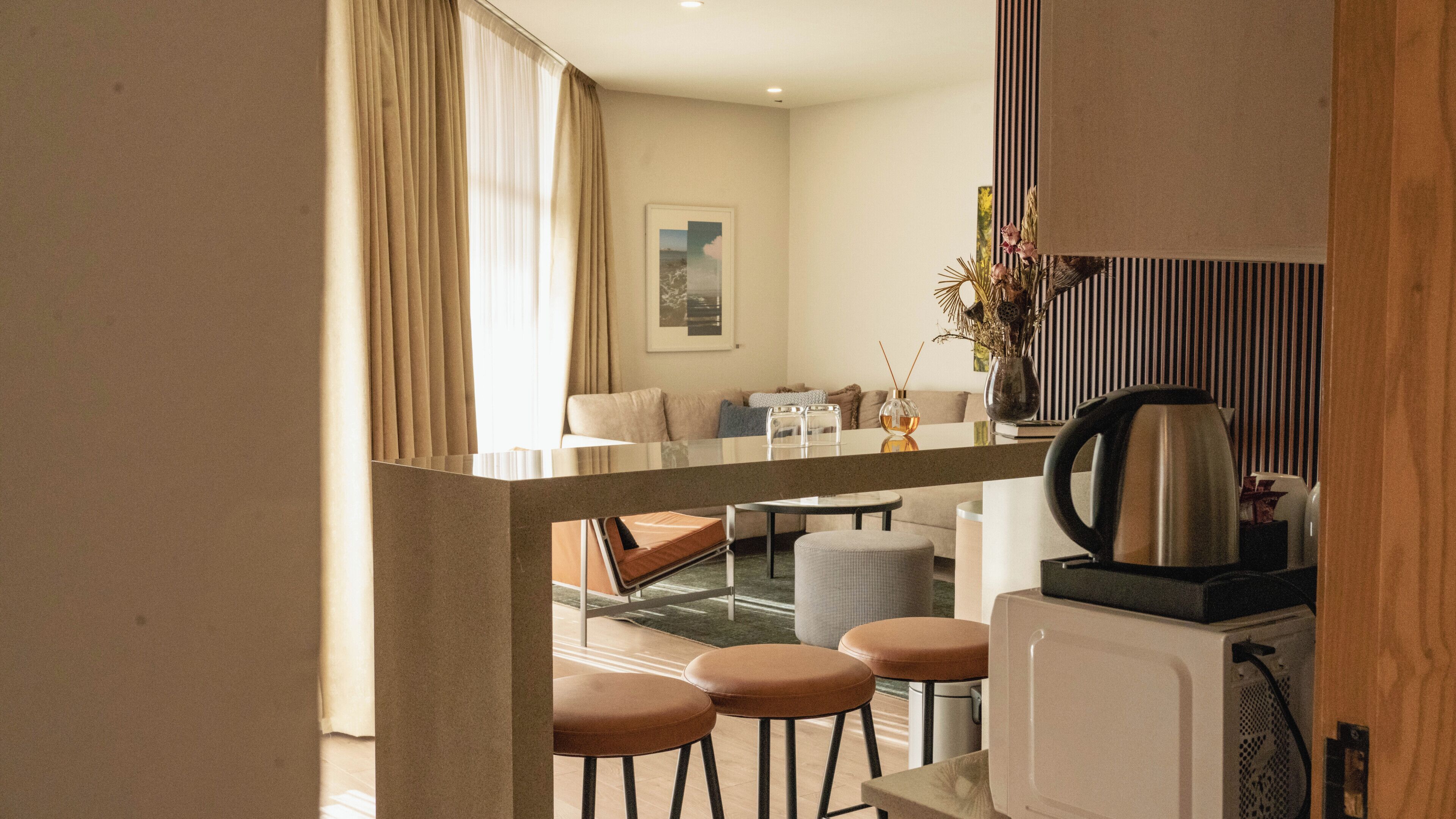 A modern hotel room with a kitchenette, a dining area with a table and chairs, and a living area with a sofa and a coffee table.