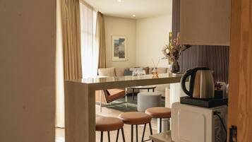 A modern hotel room with a kitchenette, a dining area with a table and chairs, and a living area with a sofa and a coffee table.