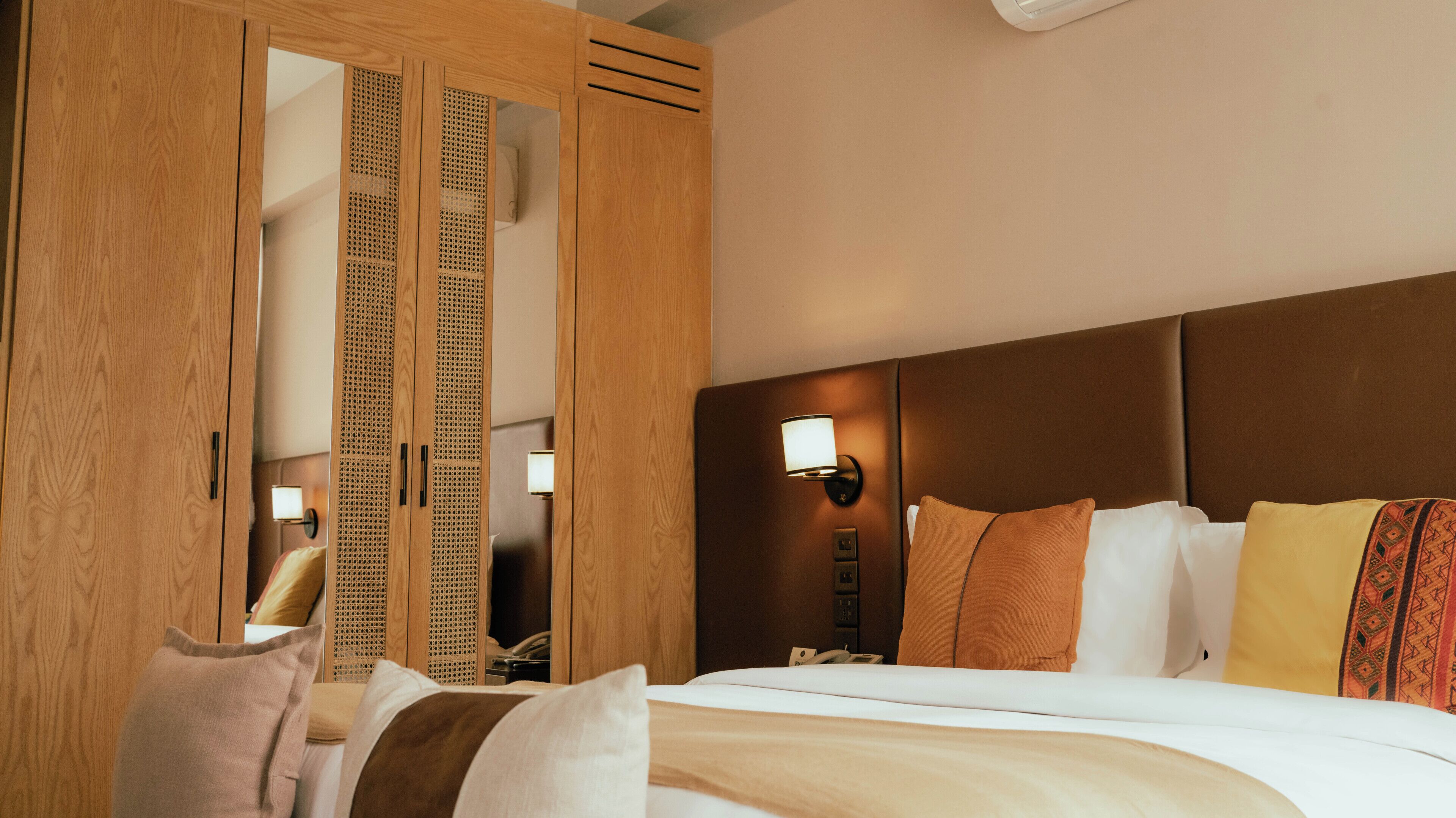 Une chambre d’hôtel avec une grande armoire en bois, un lit avec plusieurs oreillers, une table de chevet avec une lampe et un luminaire fixé au mur.