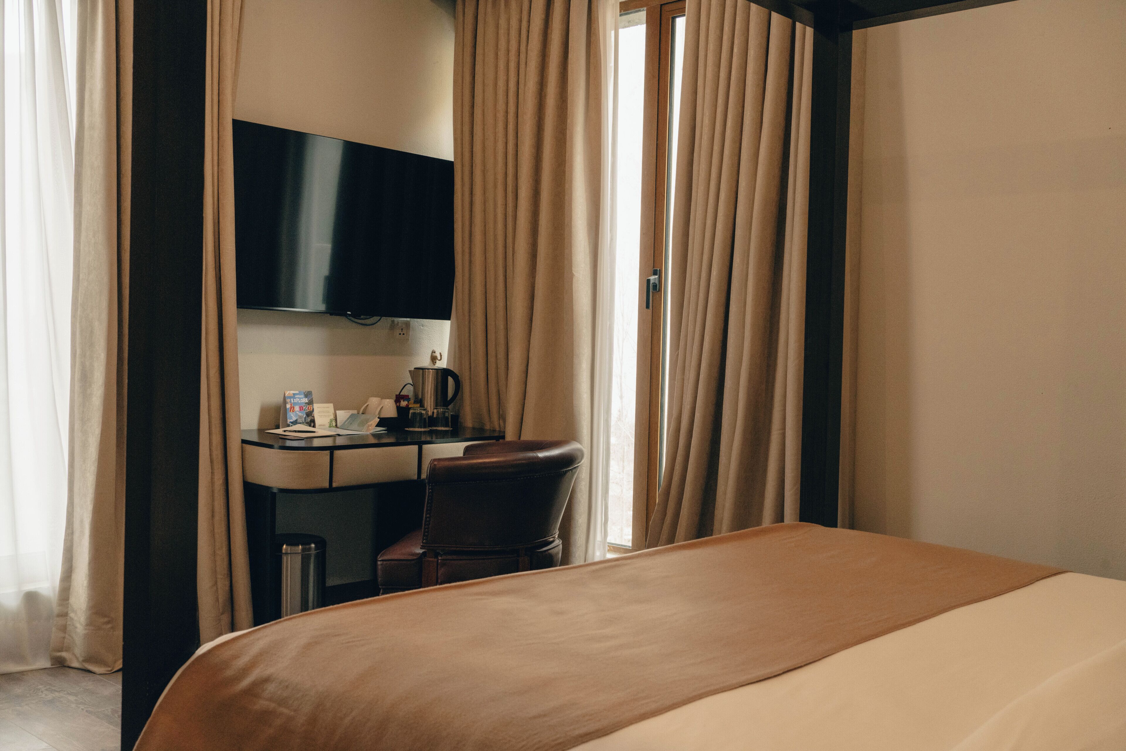 Ein Hotelzimmer mit Bett, Schreibtisch, Stuhl, Fernseher und Vorhängen.