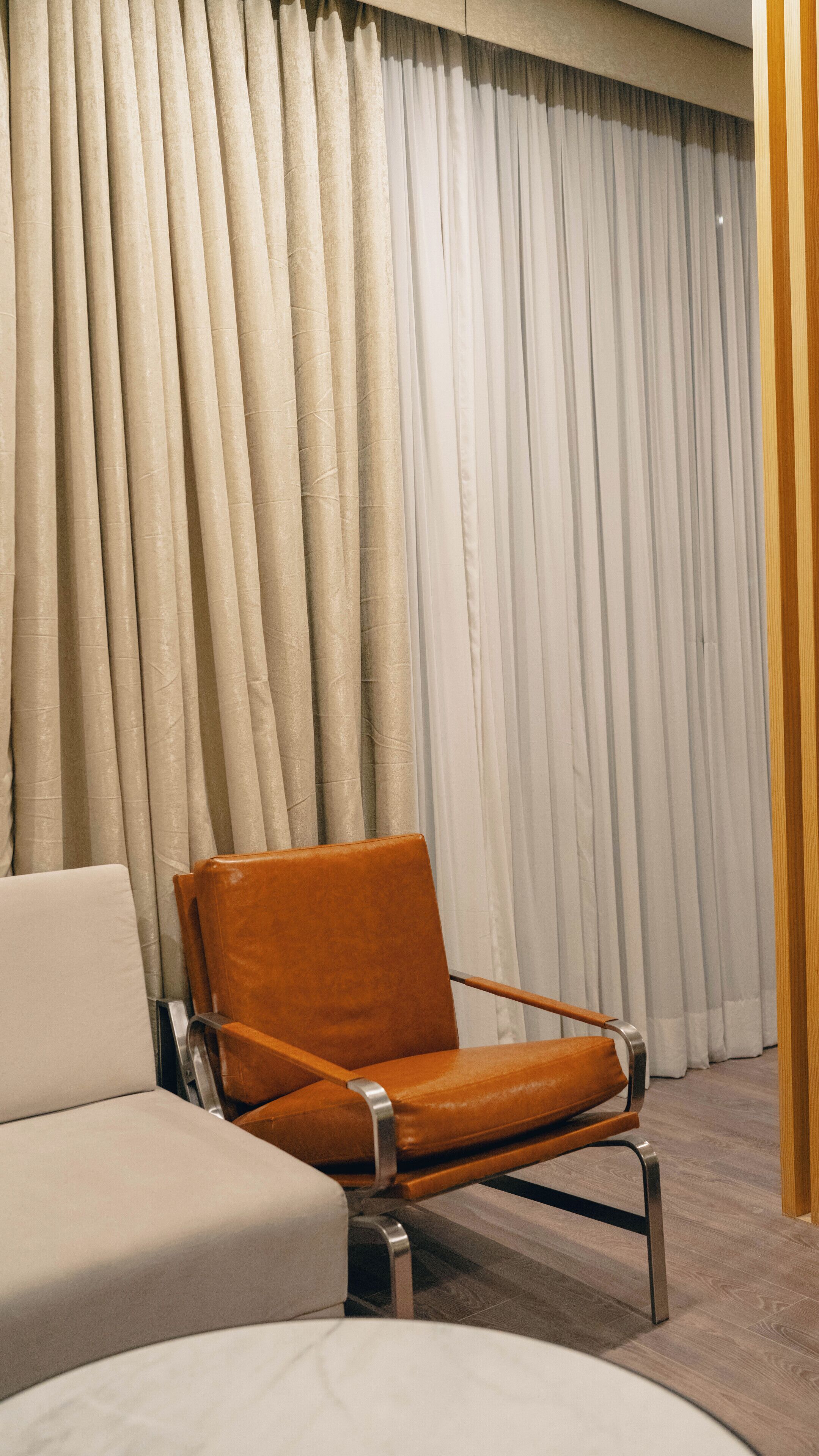 A modern room with a leather armchair, a sofa, and a large window with curtains.