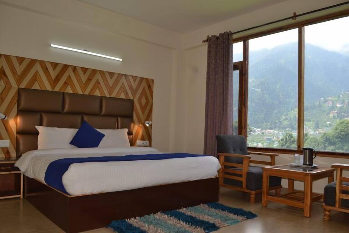 A hotel room with a large bed, a view of mountains, and a wooden table with chairs.