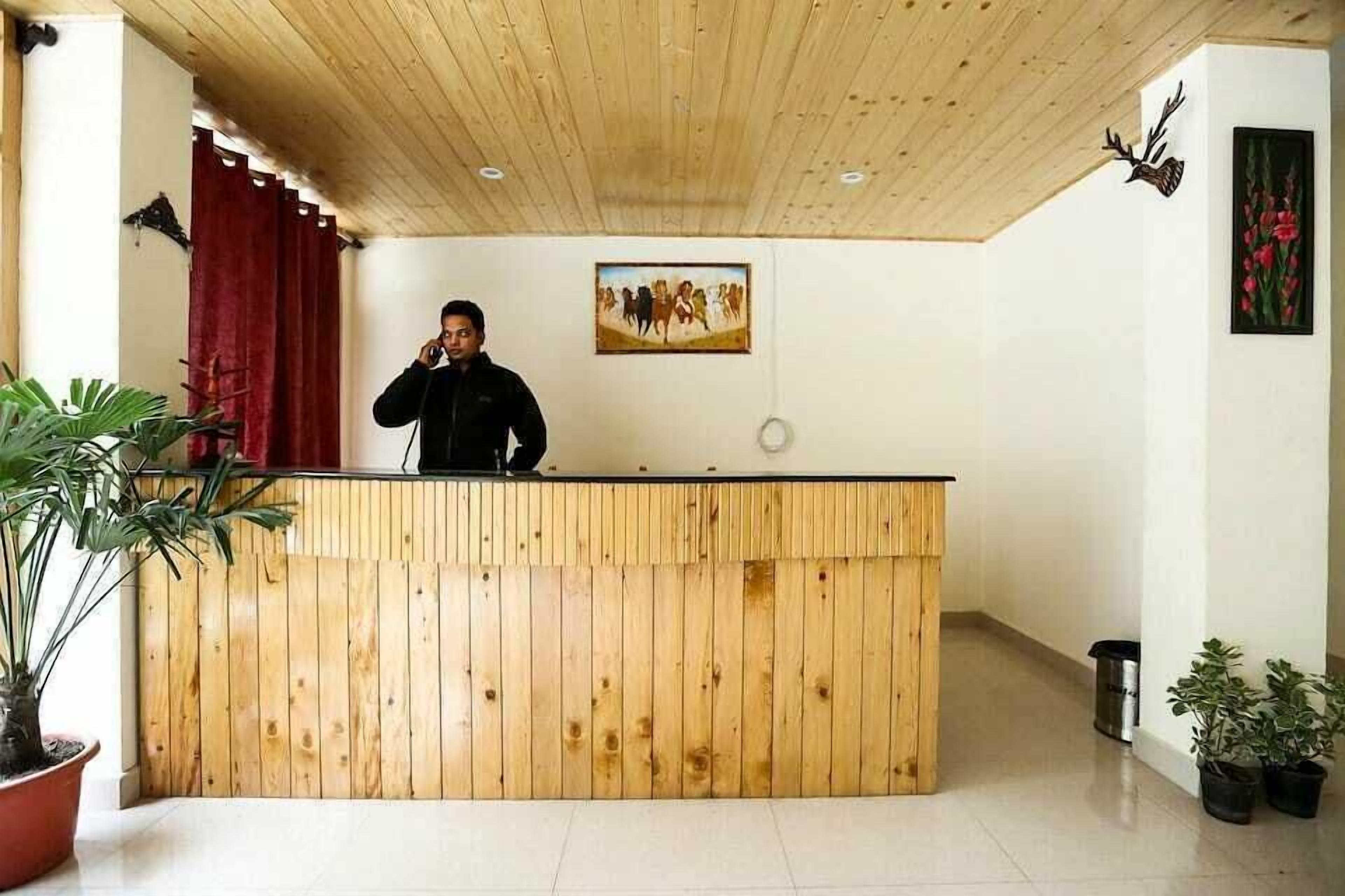 A reception desk with a wooden finish, a painting above it, and potted plants around.
