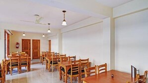 A spacious dining area with wooden tables and chairs, ceiling fans, and pendant lights.
