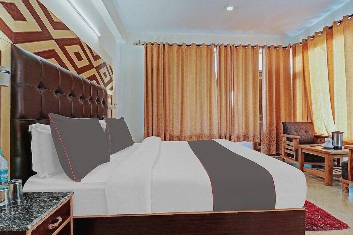 A hotel room with a large bed, a wooden headboard, a small table with a lamp, and curtains.