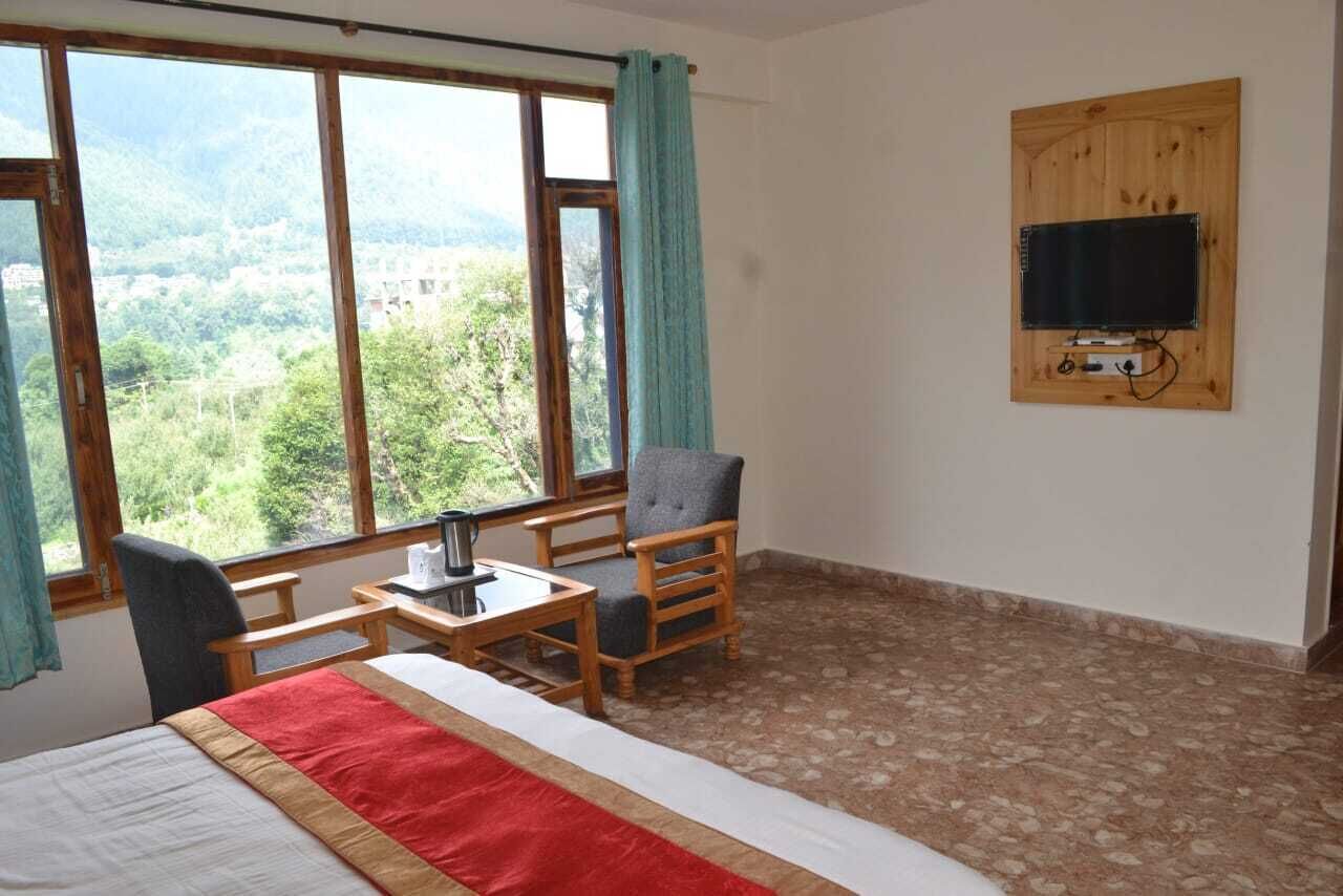 A room with a bed, a table with a kettle, a chair, and a TV mounted on the wall.