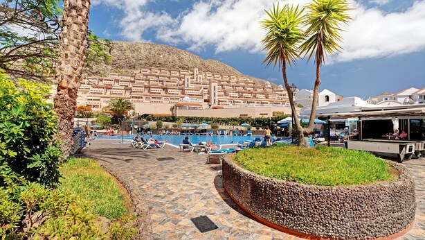 Un resort con piscina, palmeras y montañas al fondo.