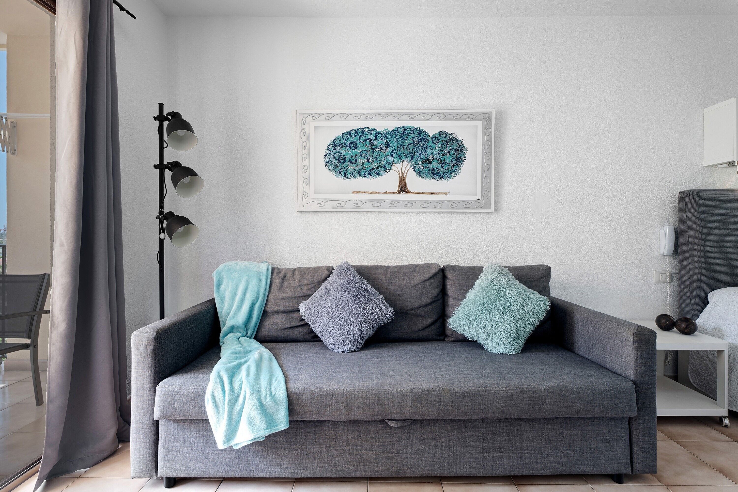 A grey sofa with three pillows, a framed tree artwork on the wall, and a floor lamp.