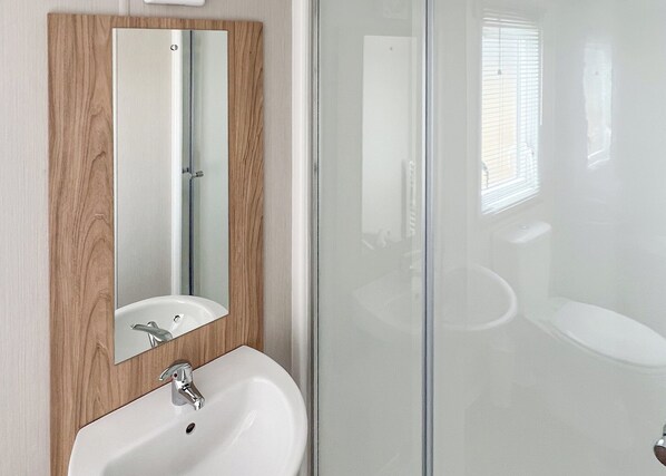 Une salle de bain avec un meuble-lavabo en bois, un lavabo blanc et une cabine de douche en verre.
