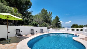 Une piscine à bord incurvé, entourée de chaises longues et d’un parasol vert.