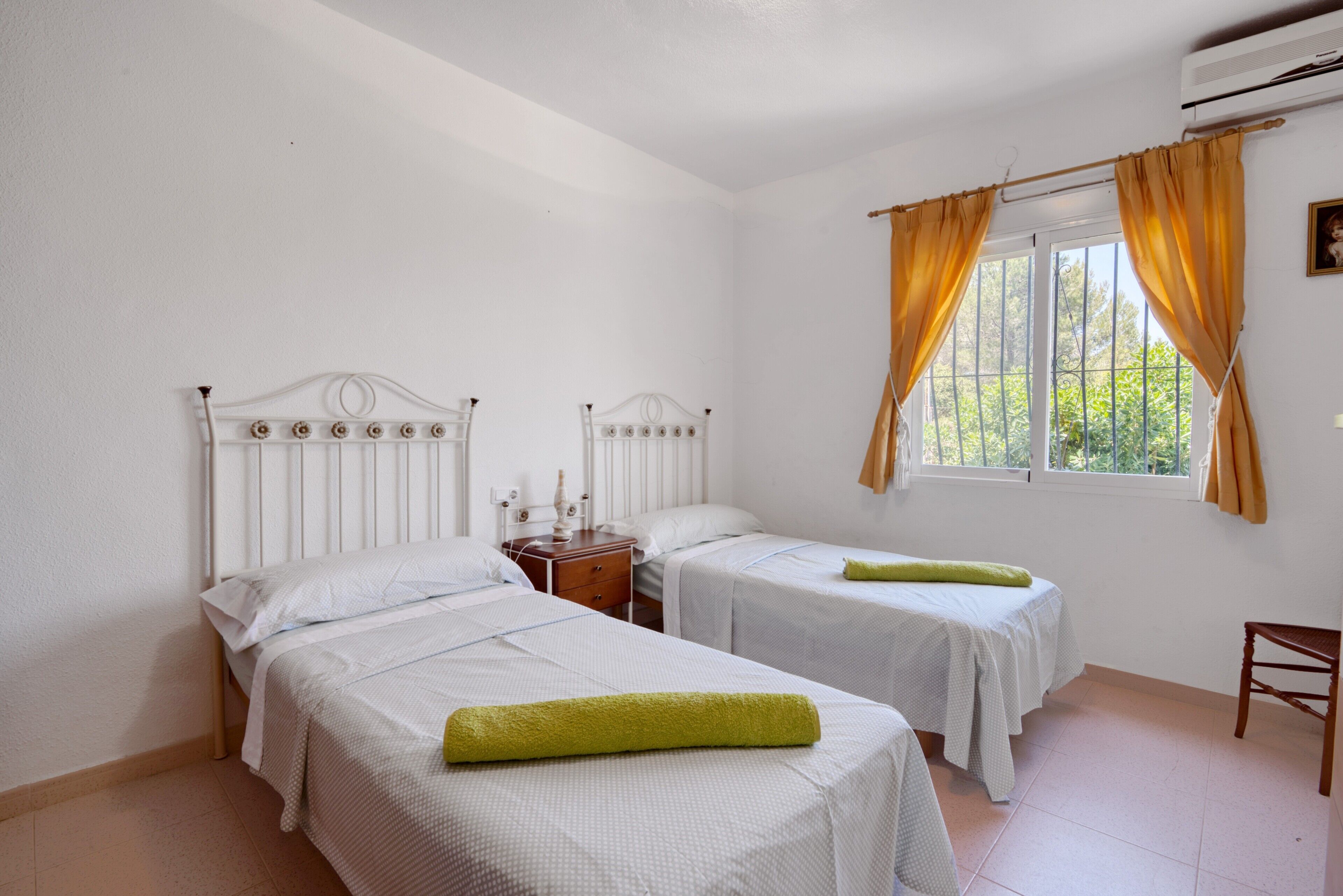 Ein Zimmer mit zwei Betten, einem Nachttisch, einem Fenster mit Vorhängen und einem Sessel.