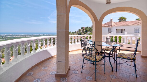 Un balcon avec une table et des chaises, une vue sur la mer et un bâtiment en arrière-plan.