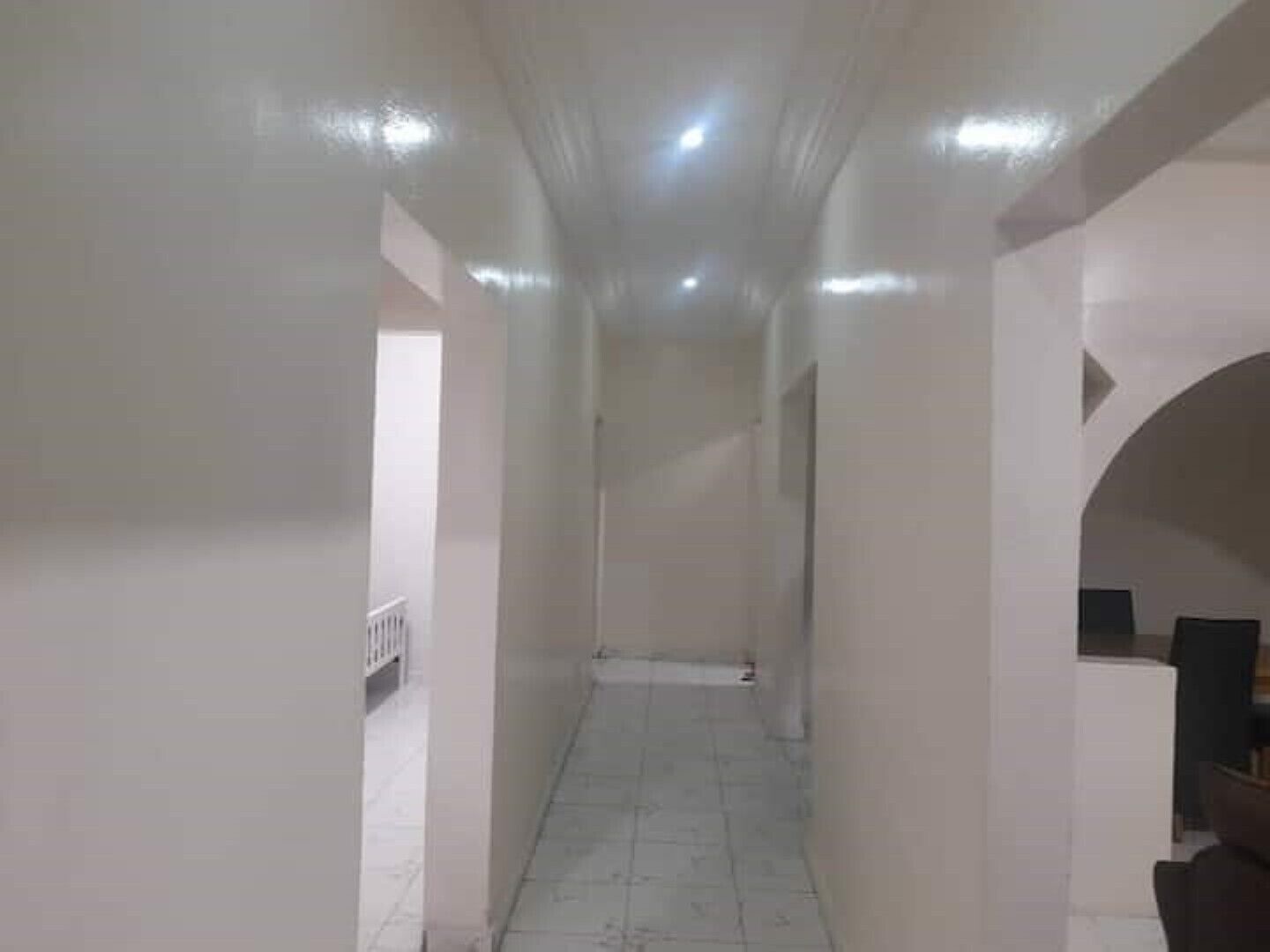 A narrow hallway with white walls and a tiled floor, leading to a door at the end.