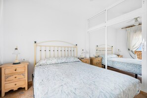 A bedroom with a bed, two bedside tables, a mirror, and a ceiling fan.