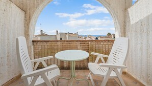 Un balcon avec une table blanche et deux chaises blanches, une arche et une vue sur les bâtiments et le ciel.
