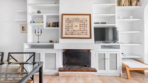 Un salon moderne avec une cheminée, des étagères blanches, une table basse en verre et un téléviseur.