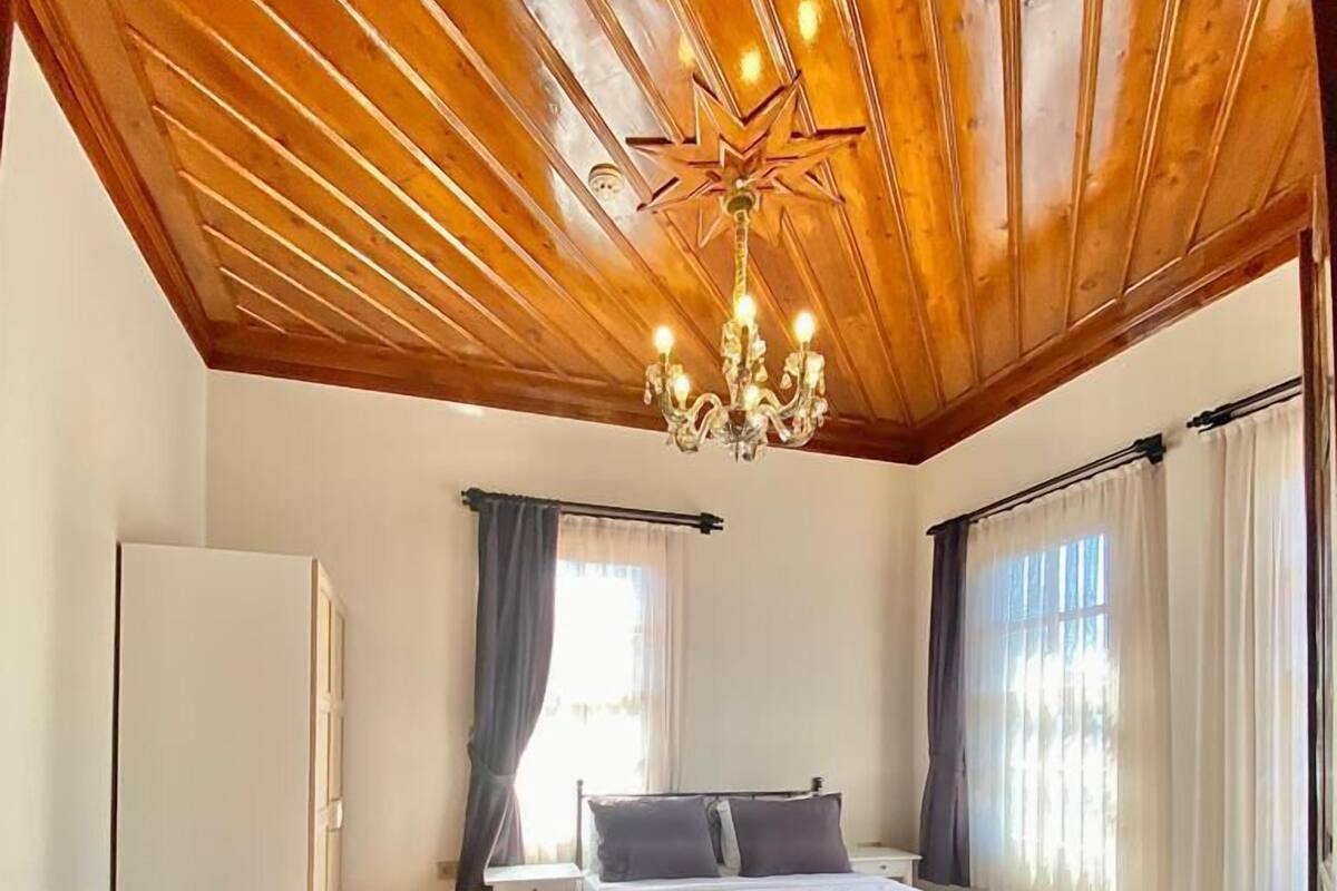 A bedroom with a wooden ceiling, a bed, a nightstand, a dresser, and a window with curtains.