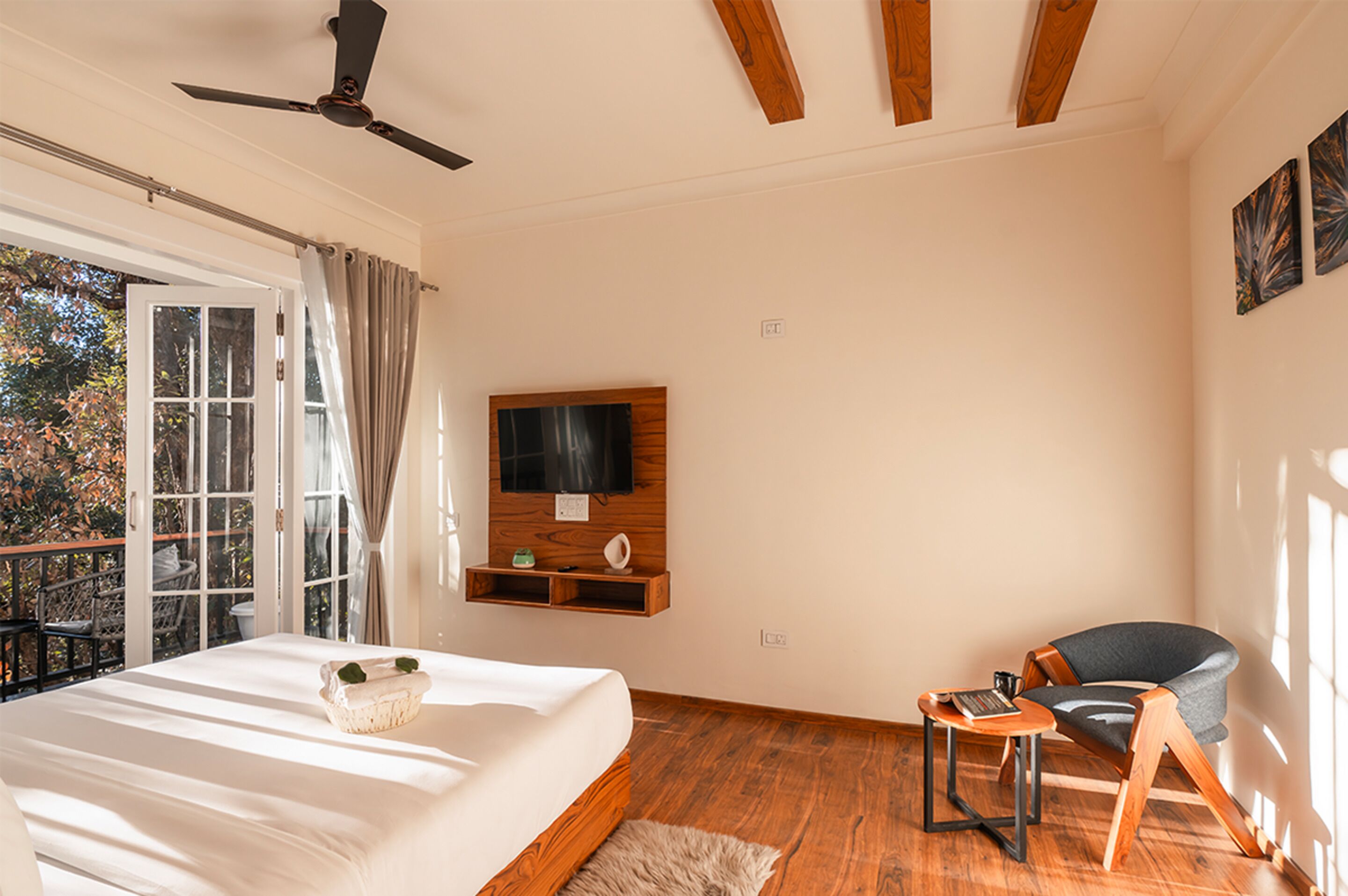Un dormitorio con cama, televisión montada en la pared, una silla y un balcón con vistas a árboles.
