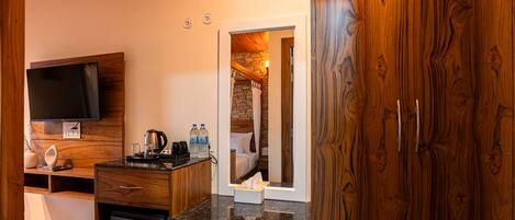 A compact hotel room with a kitchenette, a flat-screen TV, a small refrigerator, and a wooden wardrobe.