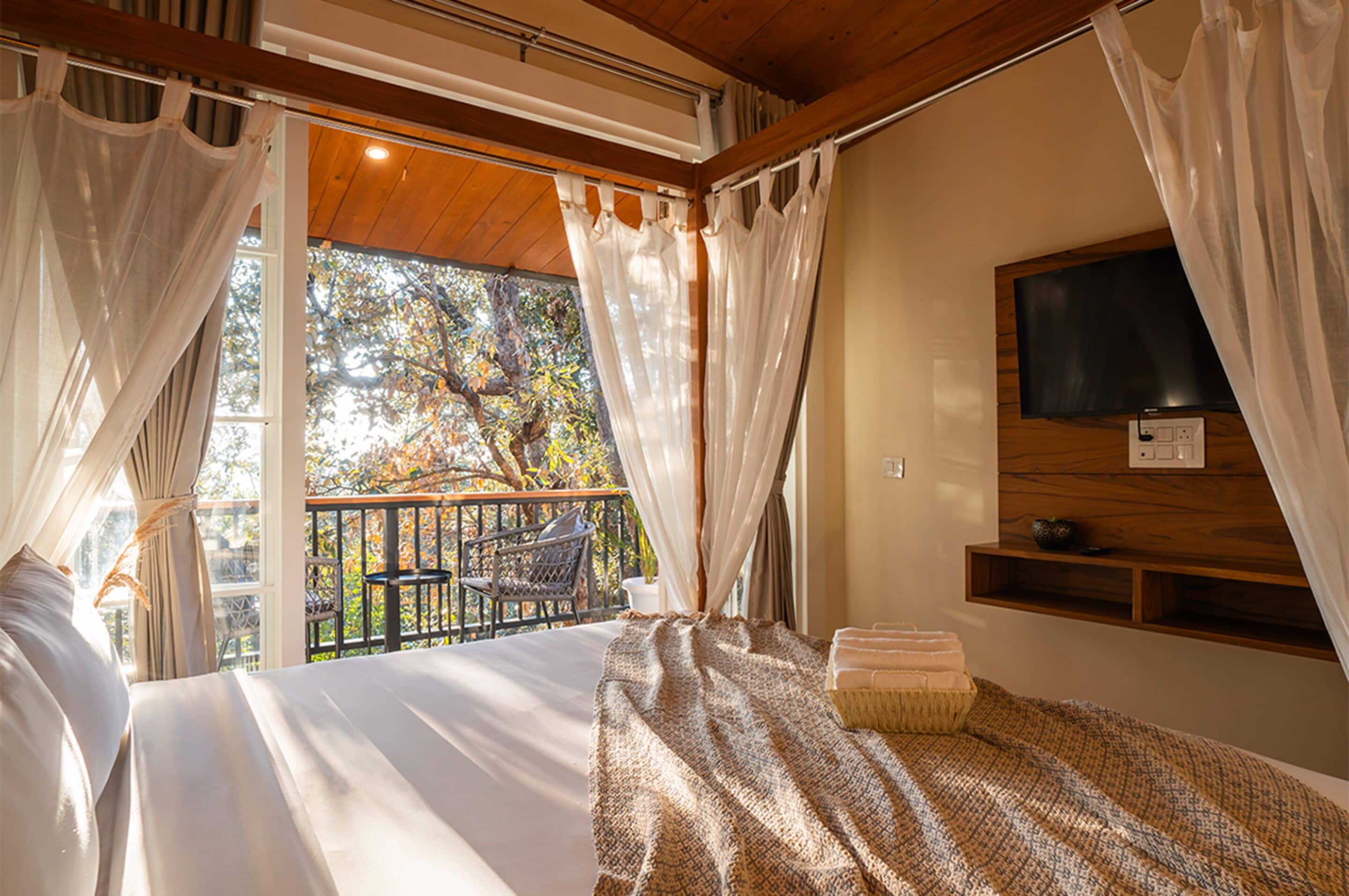 Quarto com cama, televisão na parede e varanda com cadeira e mesa.
