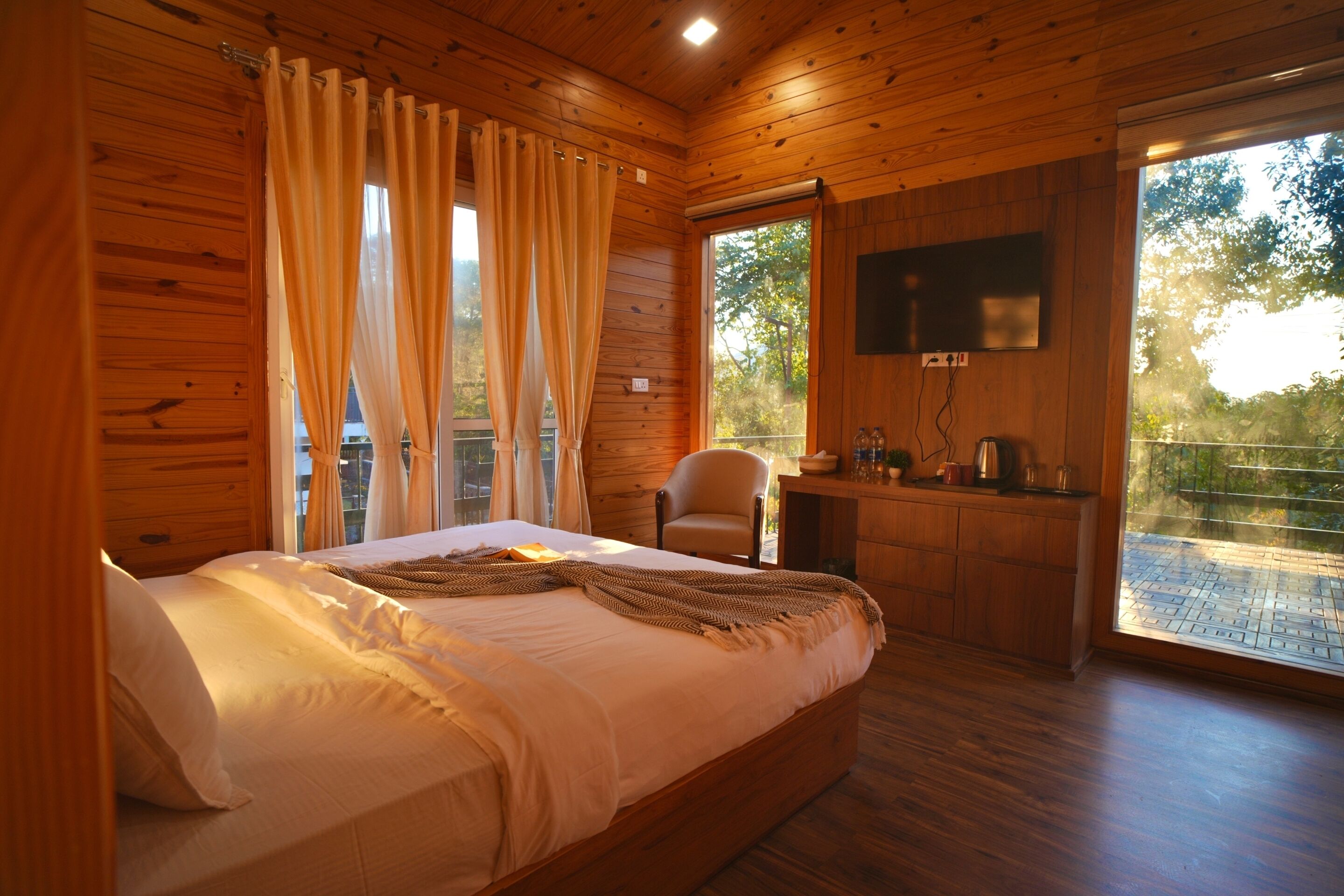 A wooden cabin bedroom with a bed, curtains, a TV, and a desk with a chair.