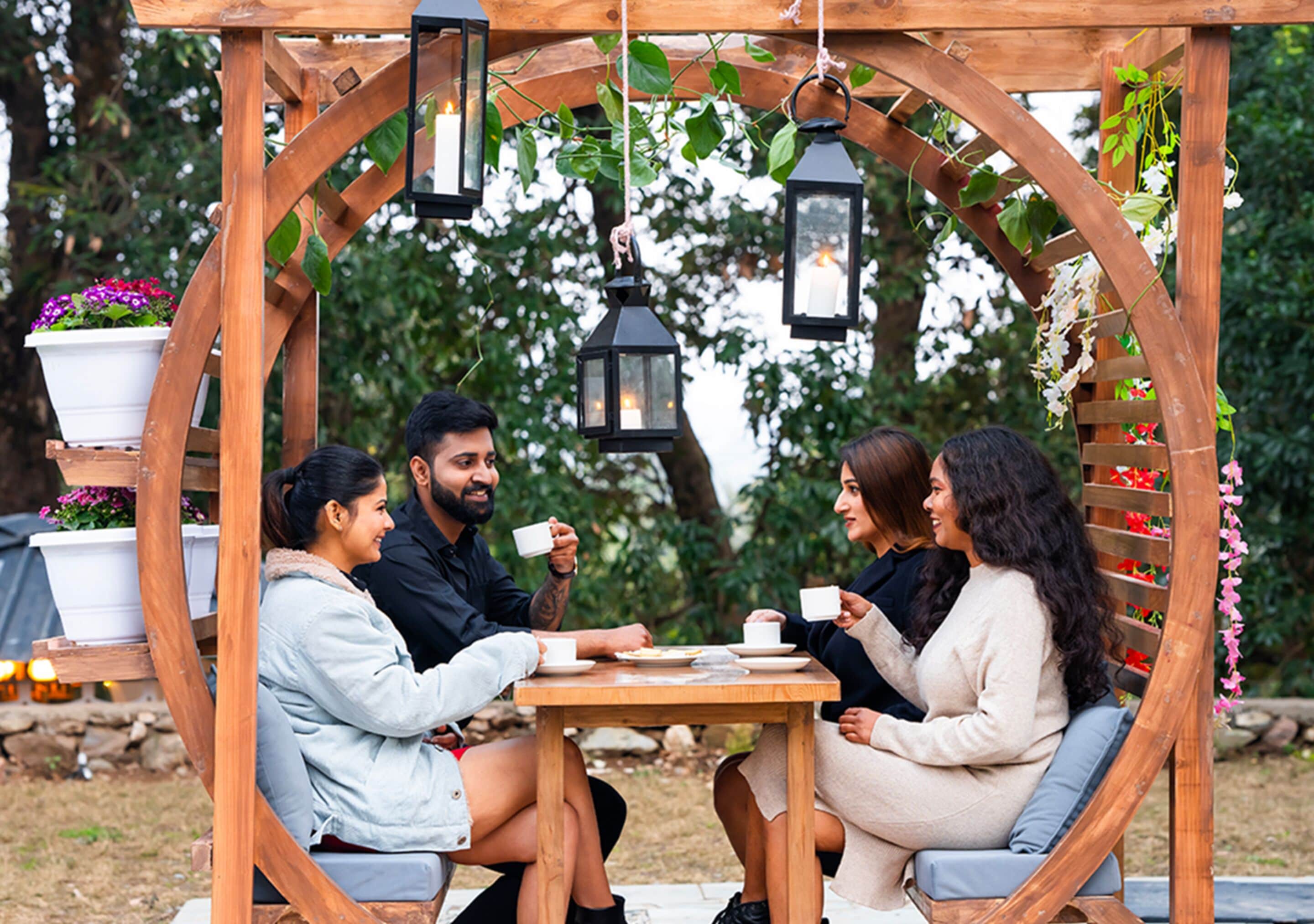 Eine Holzpergola mit hängenden Laternen, einem Tisch und Stühlen in einem Garten.