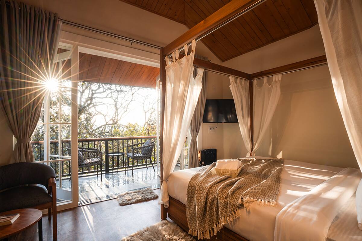 Ein Schlafzimmer mit Bett, Sessel, Fernseher und einem Balkon mit Sitzgelegenheit.