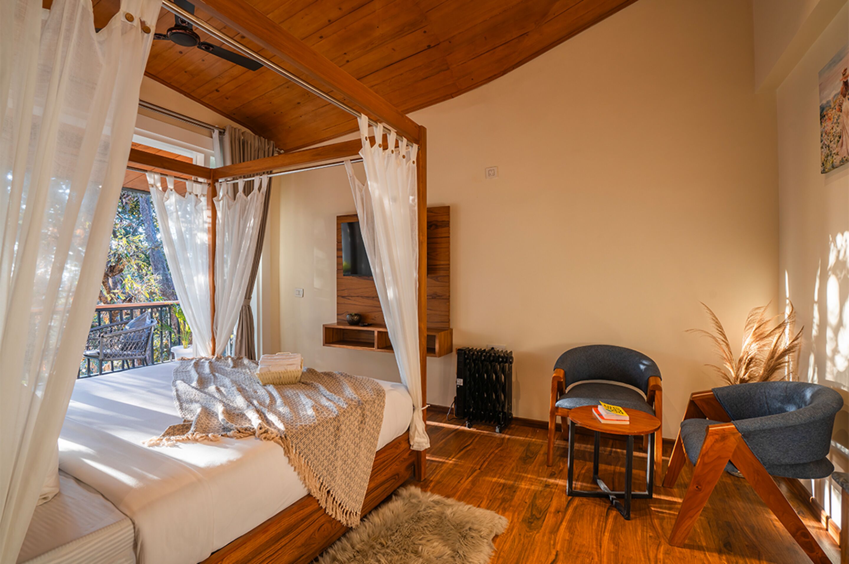 A bedroom with a wooden ceiling, a bed with a canopy, a chair, a small table, and a view of the outdoors.