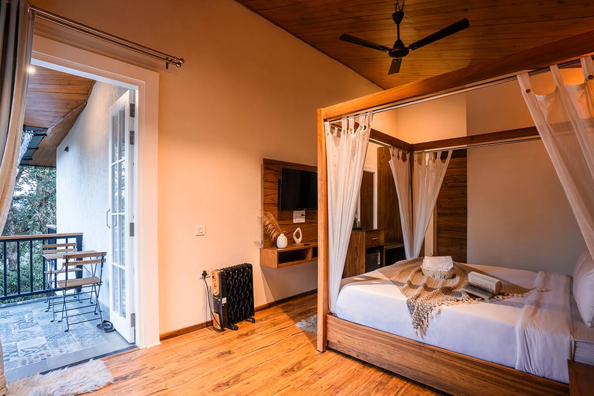 Ein Schlafzimmer mit einem Himmelbett, einem hölzernen Deckenventilator und einer kleinen Sitzecke mit Tisch und Stühlen.