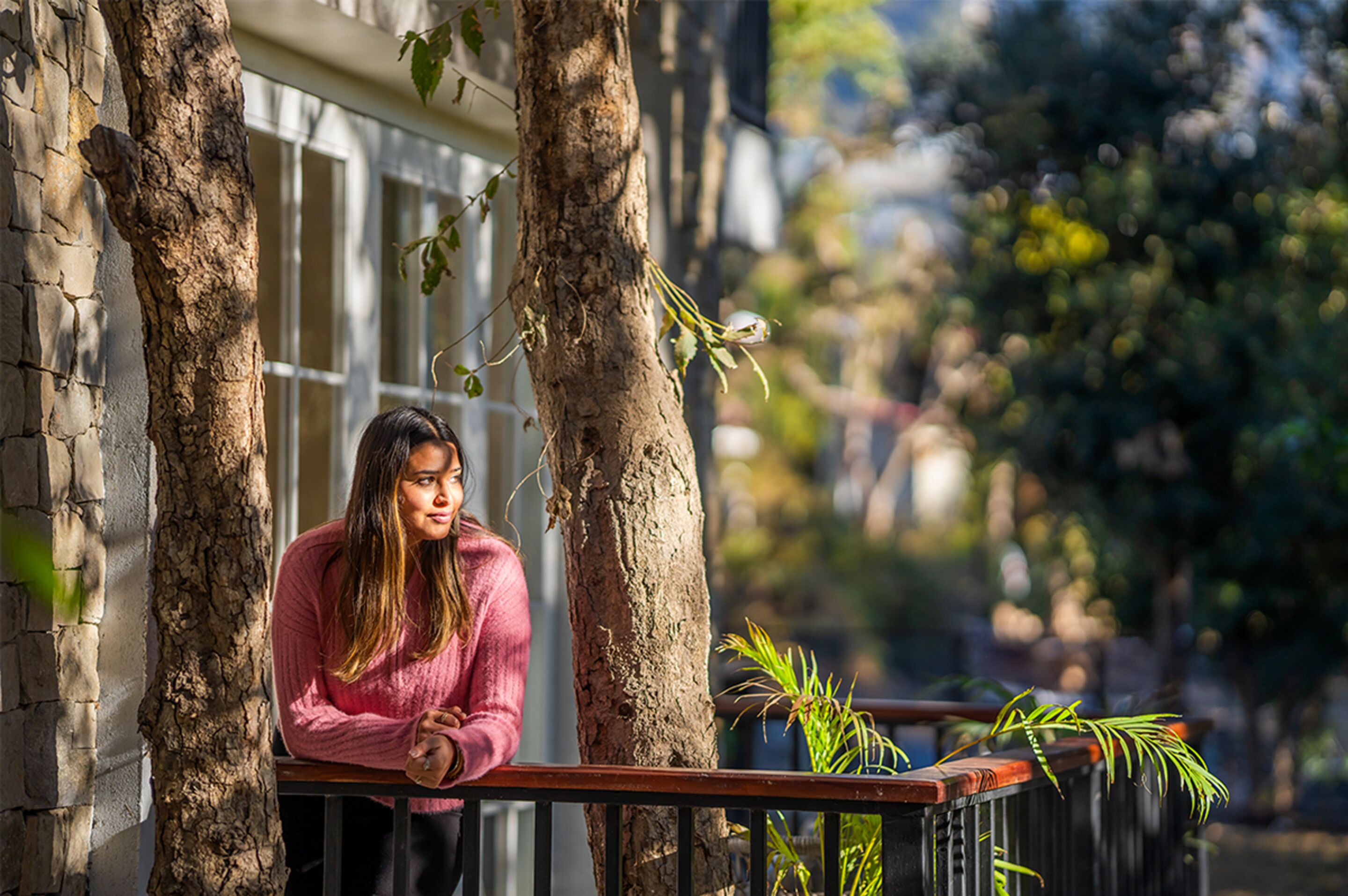 A person leaning on a balcony railing with trees and a building in the background.