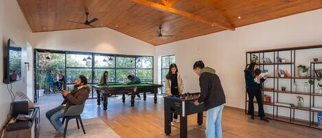 Un grand espace intérieur doté de planchers en bois, de ventilateurs de plafond, d’une table de billard et d’une table de baby-foot.