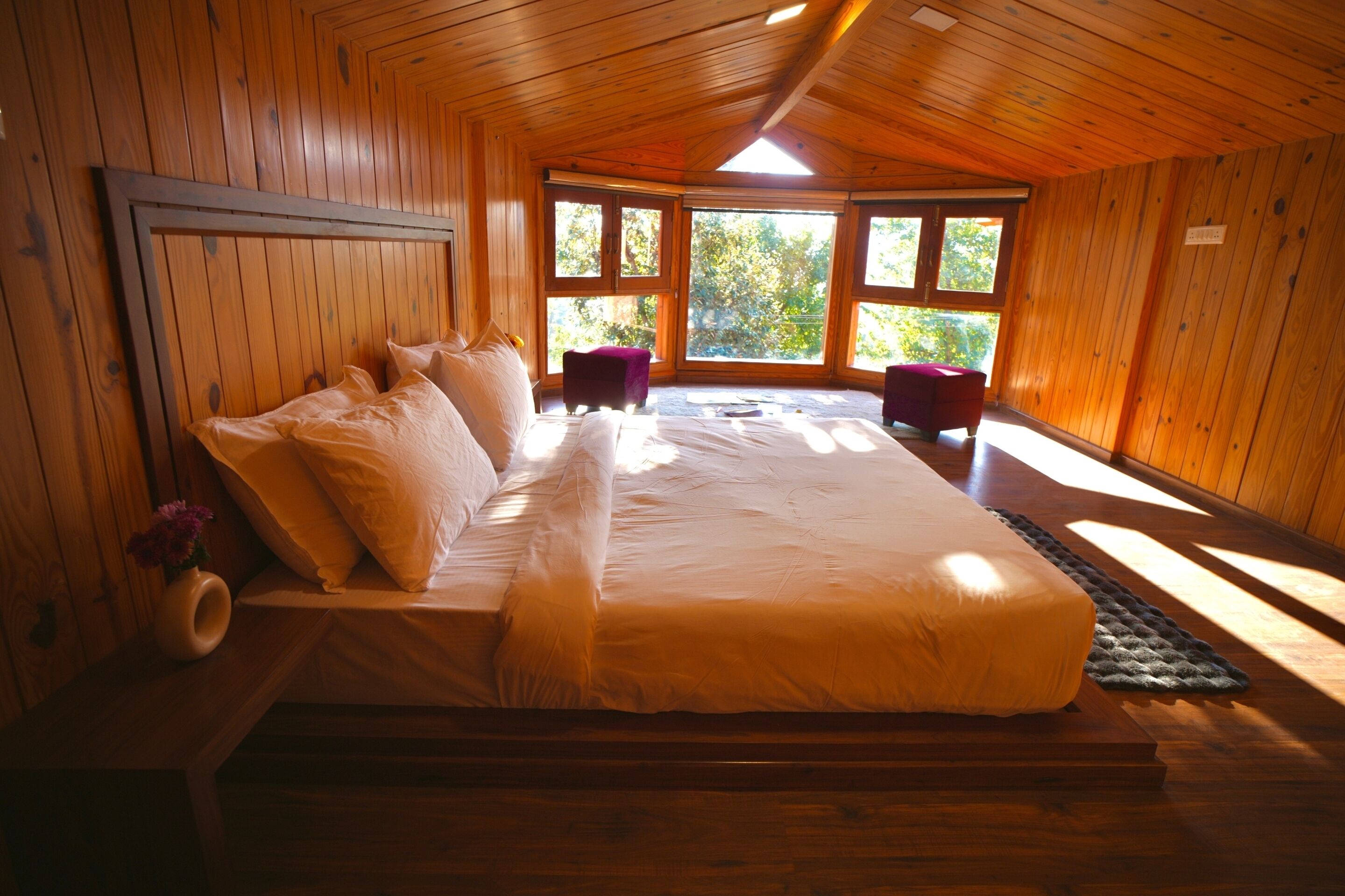 A wooden-paneled bedroom with a large bed, two chairs, and a window providing a view of greenery.