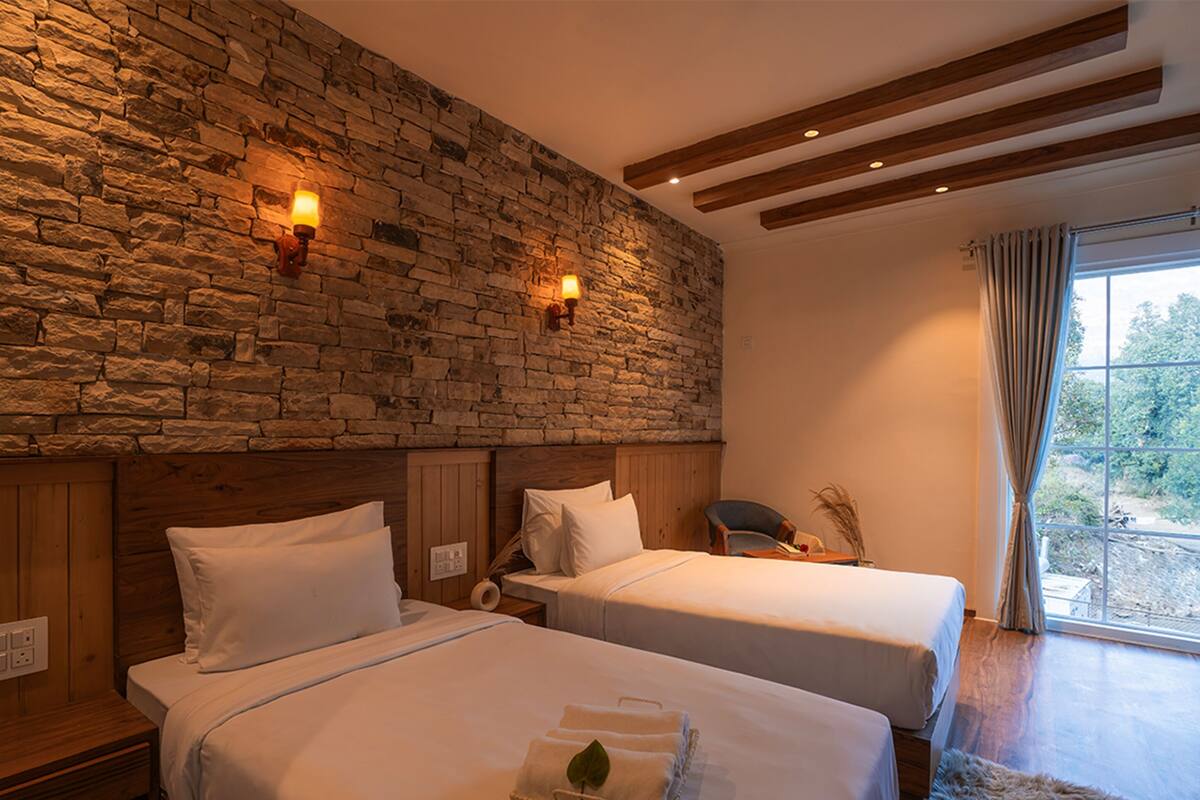 Ein Hotelzimmer mit zwei Betten, einer Steinwand, Holzbalken und einem Fenster mit Vorhängen.
