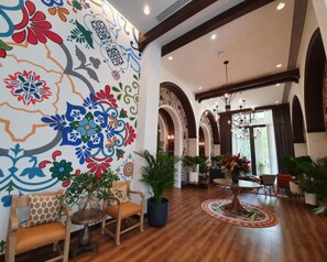 A spacious lobby with a wooden floor, a colorful mural, and a chandelier.