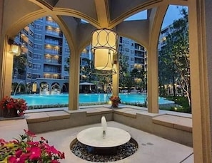A pool area with a fountain, surrounded by a covered seating area with arches and a view of a high-rise building.