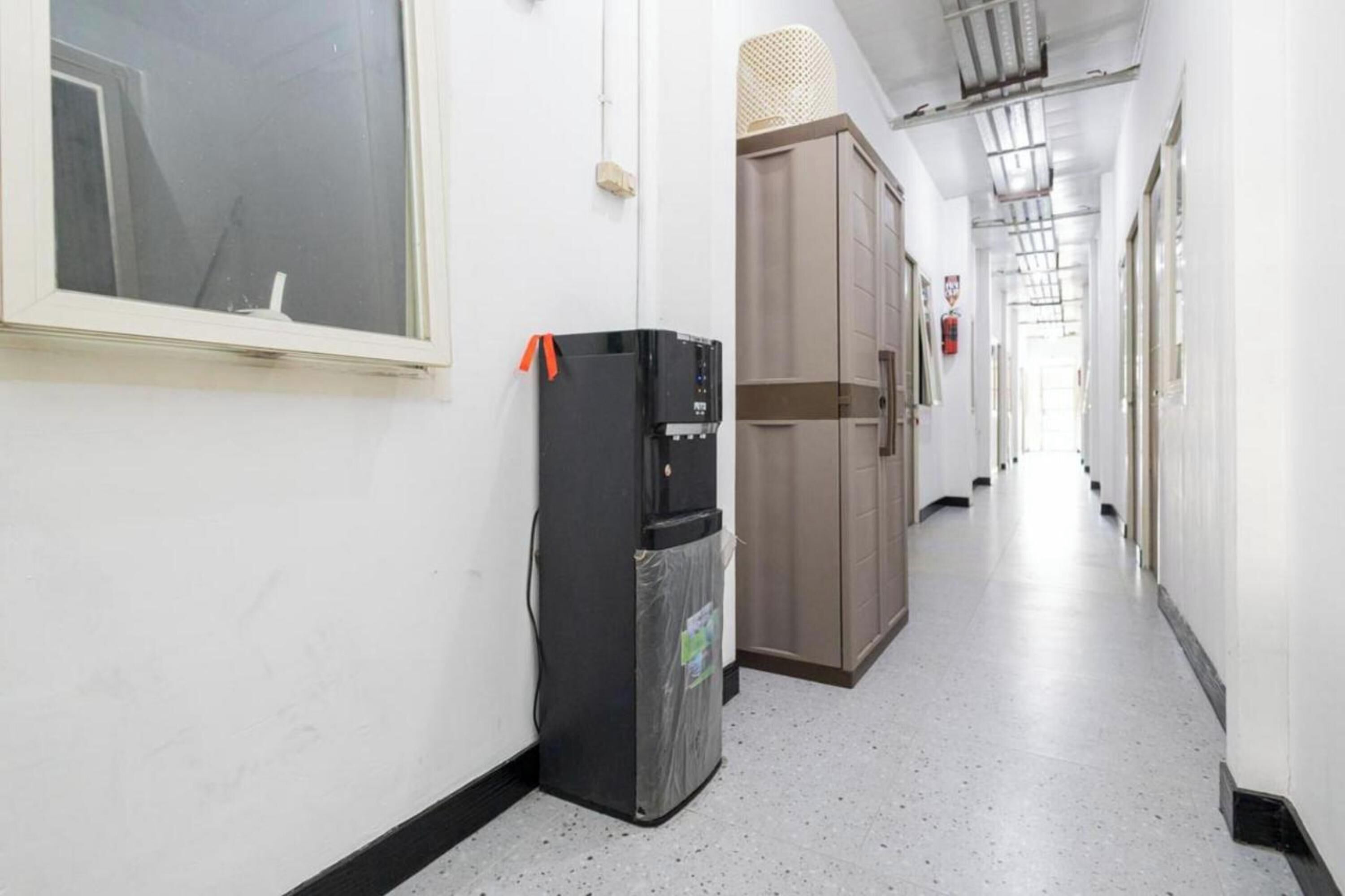 A hallway with a refrigerator, cabinets, and a window.