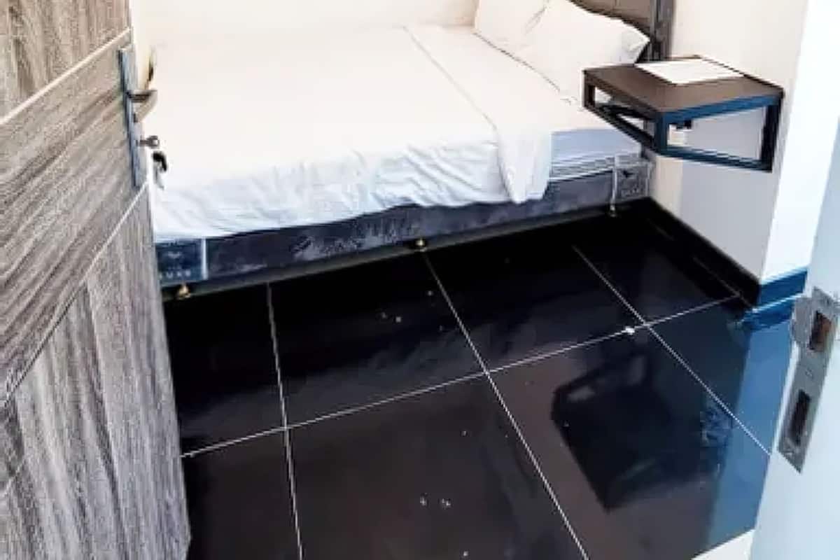 Una habitación pequeña con una cama, una mesita de noche y un aire acondicionado instalado en la pared.