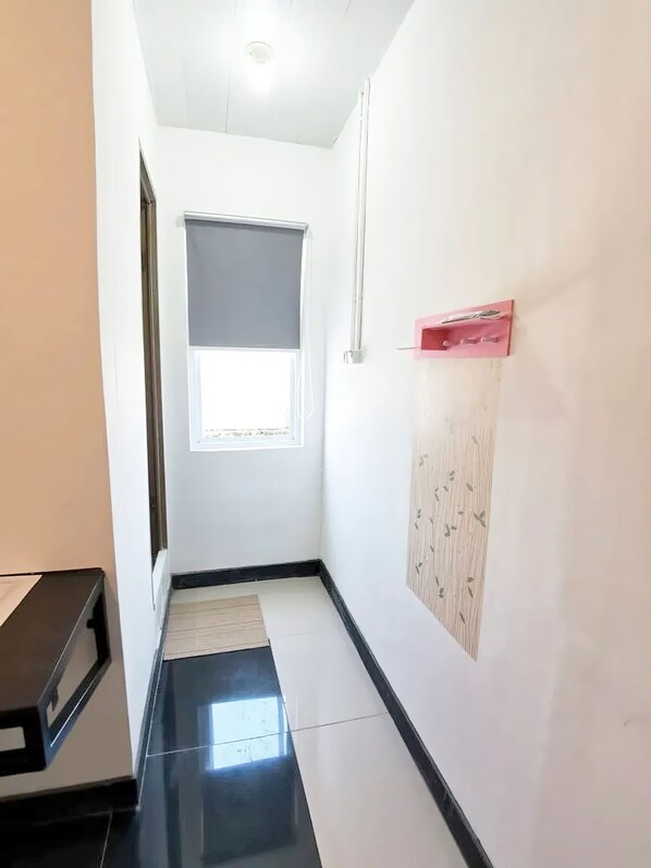 A narrow hallway with a window, a door, and a wall-mounted shelf.