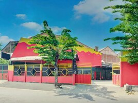 A building with a red and yellow facade, a gated entrance, and a tree in front.