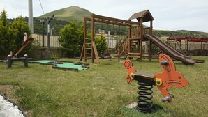 Un parque infantil con un tobogán de madera, columpios y una figura de animal sobre resortes.