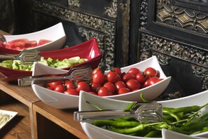 Una mesa de buffet con diversos alimentos, incluyendo tomates, pepinos y pimientos verdes.