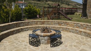Un patio de piedra con una fogata y dos sillas, rodeado por un muro de piedra.