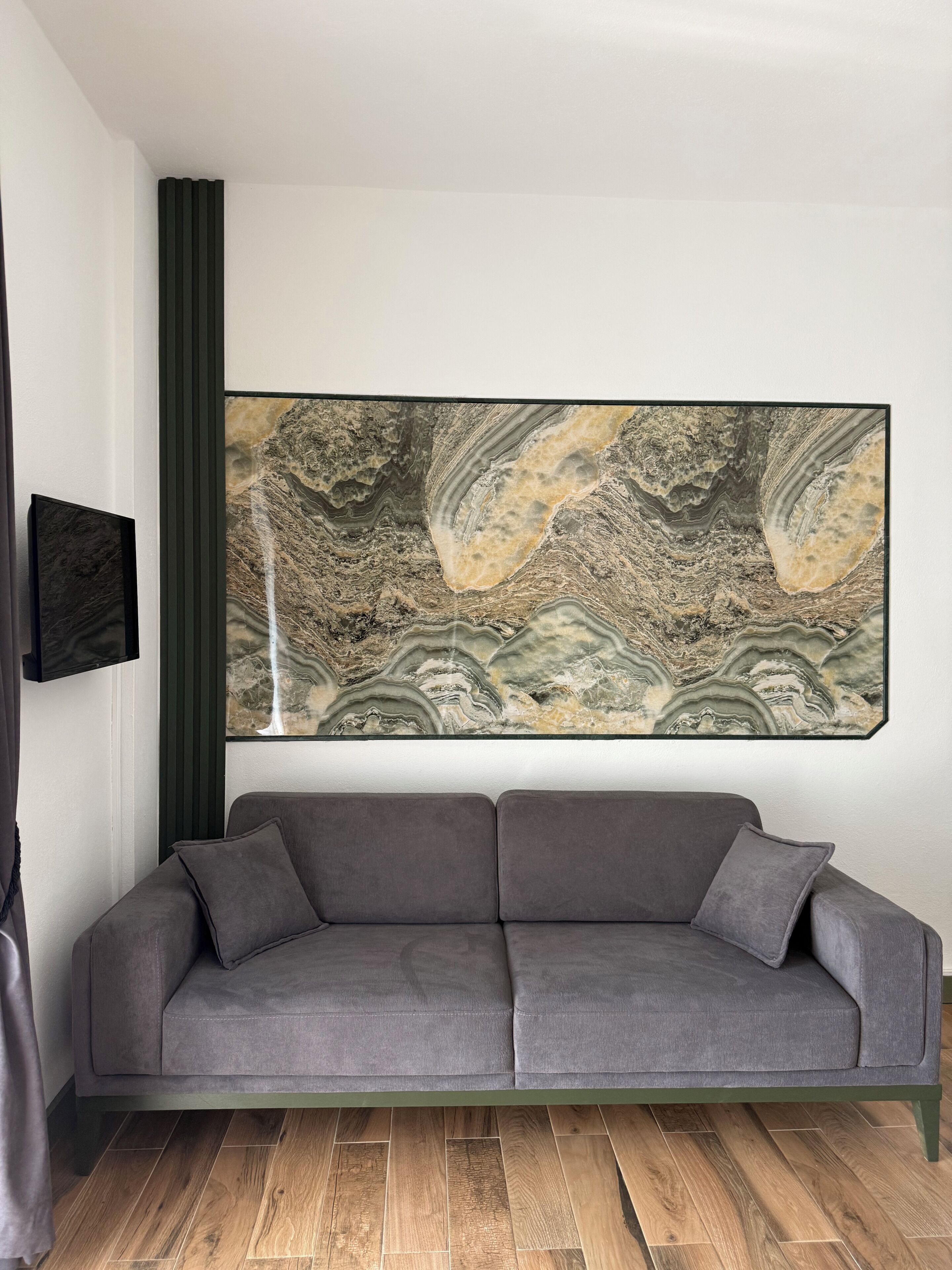 Una sala de estar moderna con un sofá gris, un cuadro abstracto grande y piso de madera.