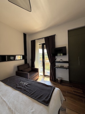 A hotel room with a bed, a sofa, a television, a desk, and a view of the outdoors. - Agios Hotel (Gökçeada)