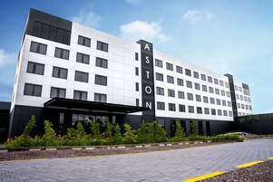 Un hotel moderno con un llamativo letrero 'ASTON', que presenta una fachada limpia y blanca con detalles negros y una entrada cubierta.